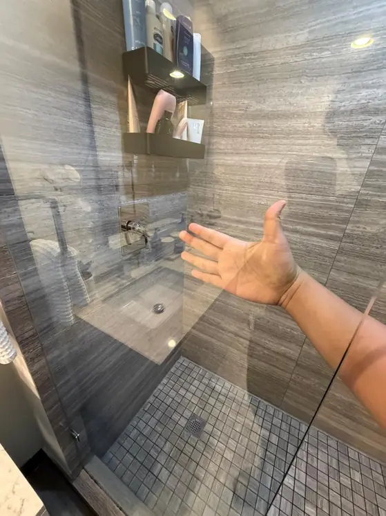 A hand behind spotless shower glass, with no streaks